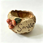 Beige ceramic planter with 'Smile' text and red flower side accents, empty.