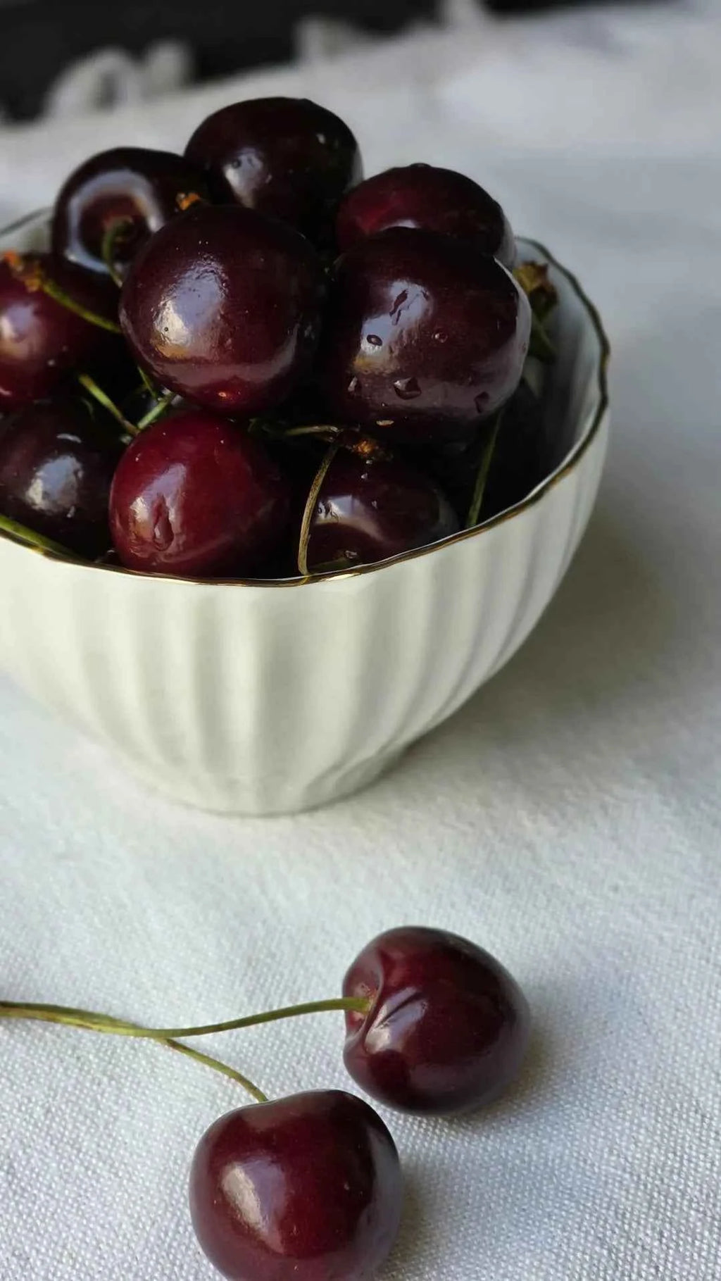 Dark red cherries in a white bowl with stems