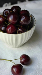 Dark red cherries in a white bowl with stems