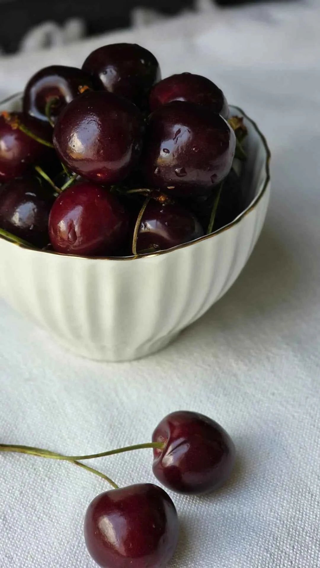 Dark red cherries in a white bowl with stems